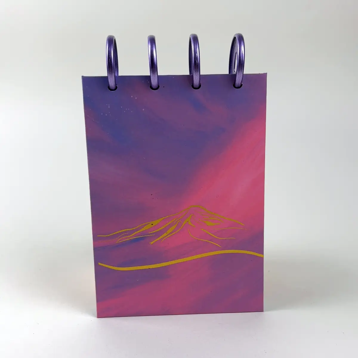 Libreta A6 Villarica Sunset con paisaje de montaña en tonos morados y rosados y discos superiores